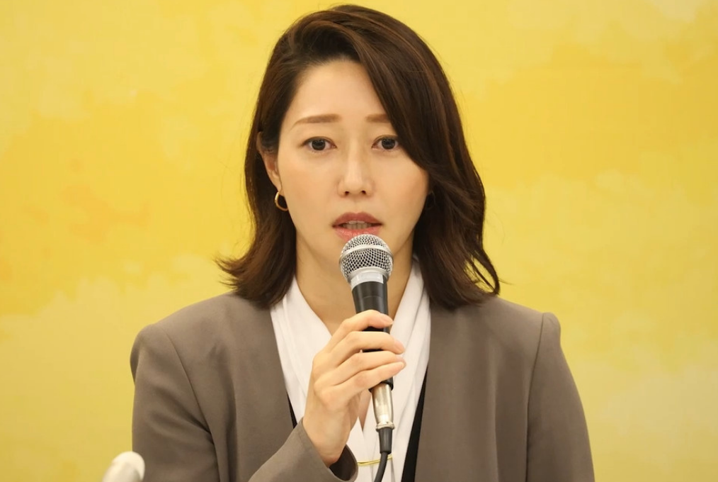 元NHKアナウンサーの牛田茉友さん。記者会見でマイクを手に、真剣な表情で話をしている様子。